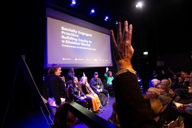 A group of people sit, some with their hands raised, in a workshop