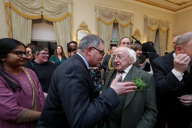 A man wearing glasses leans in to speak to the President of Ireland, Michael D Higgins in a large ornately decorated room