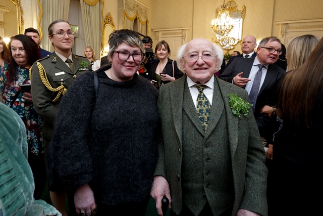 A women stands with President of Ireland, Michael D Higgins, in a large ornately decorated room