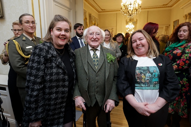 Two women stand with President of Ireland, Michael D Higgins, in a large ornately decorated room