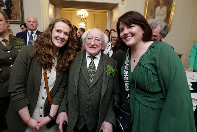 Two women stand with President of Ireland, Michael D Higgins, in a large ornately decorated room