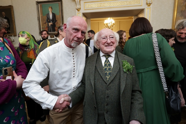 A man shakes the hand of President of Ireland, Michael D Higgins, in a large ornately decorated room