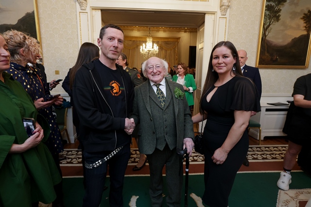 A man and a woman stand with President of Ireland, Michael D Higgins, in a large ornately decorated room