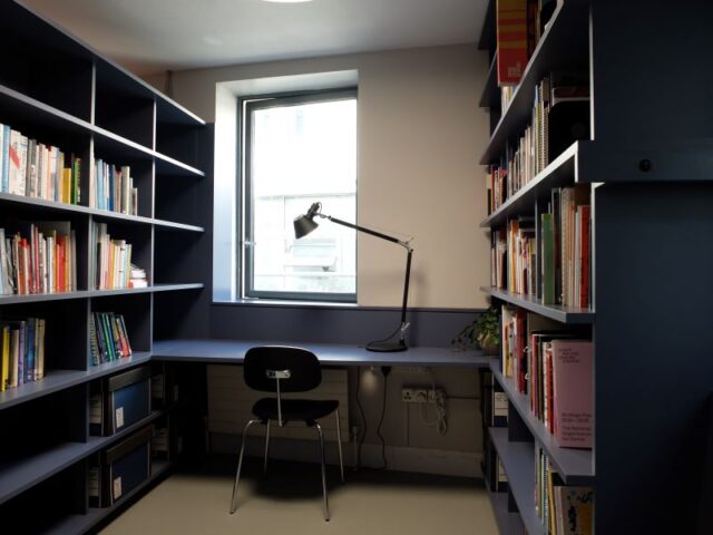 The Create reading room - navy bookshelves with a blue floor. A desk is featured, with a black lamp.