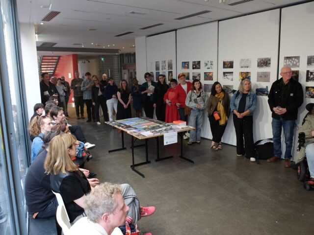 A group of people standing and sitting, each looking in one direction towards someone who is speaking